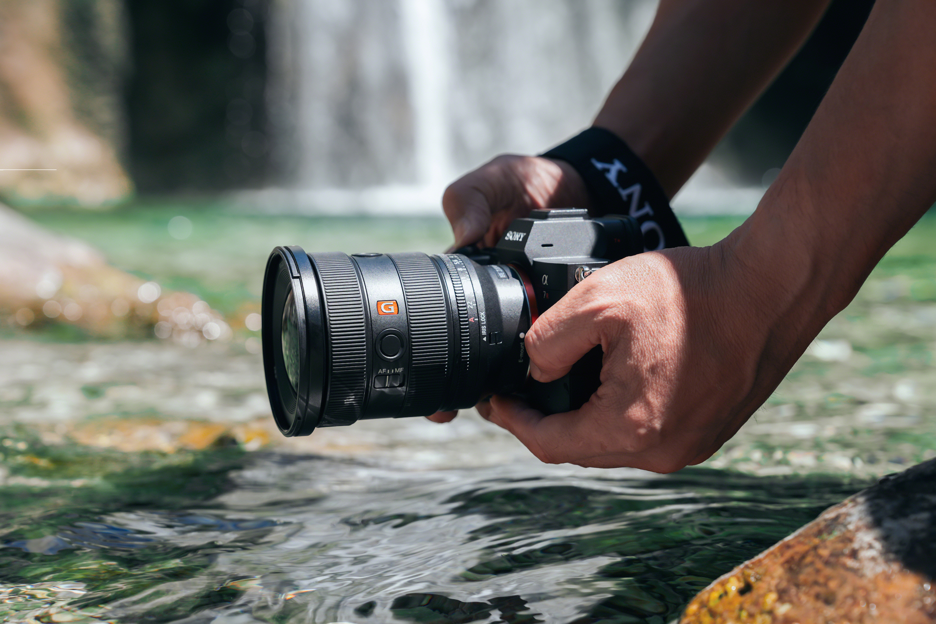 User standing at the edge of a rock and lowering their Sony gear over the water to shoot