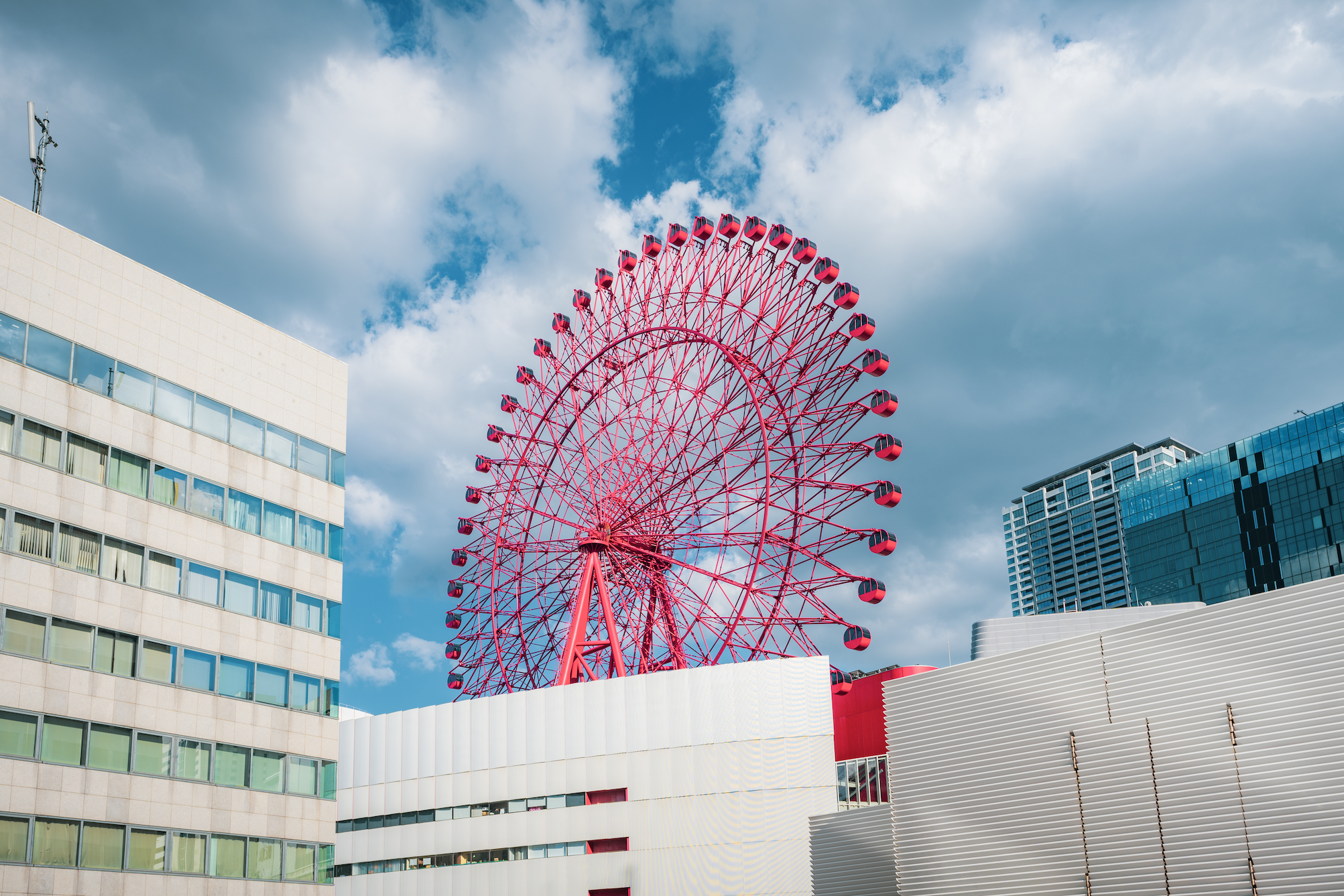 Red Hep Five ferris wheel surrounded by buildings around it against a cloudy blue sky