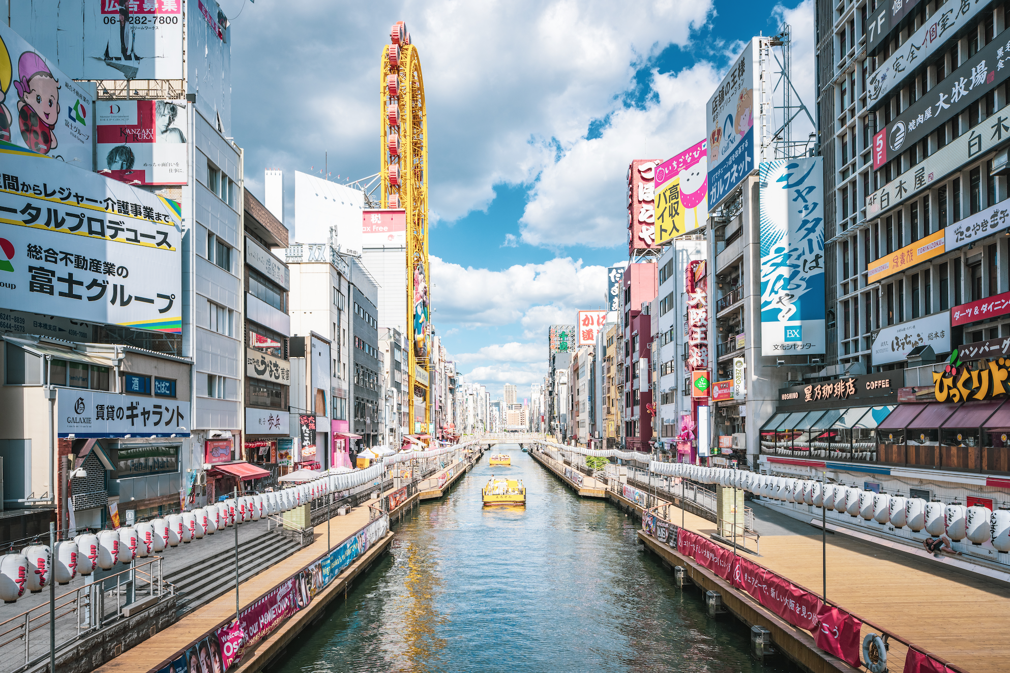 Wide shot of Dotonbori with tall buildings on either side of the canal on a sunny day