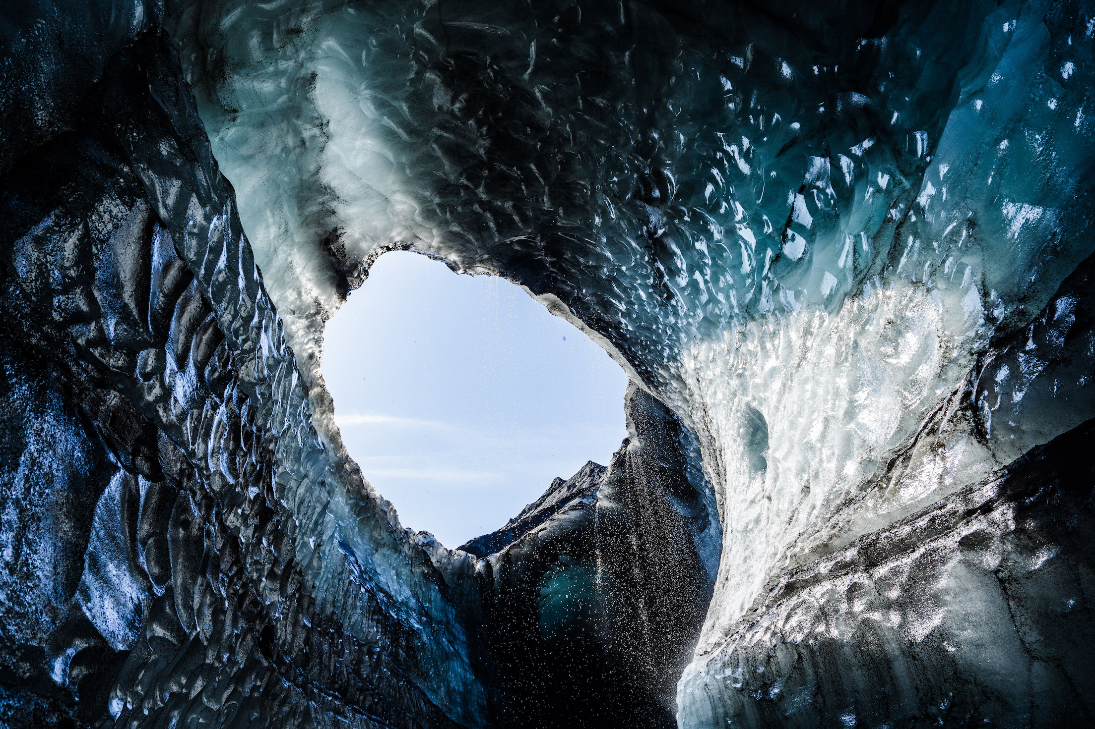 Looking up from inside of an ice cave with uneven surfaces and water trickling