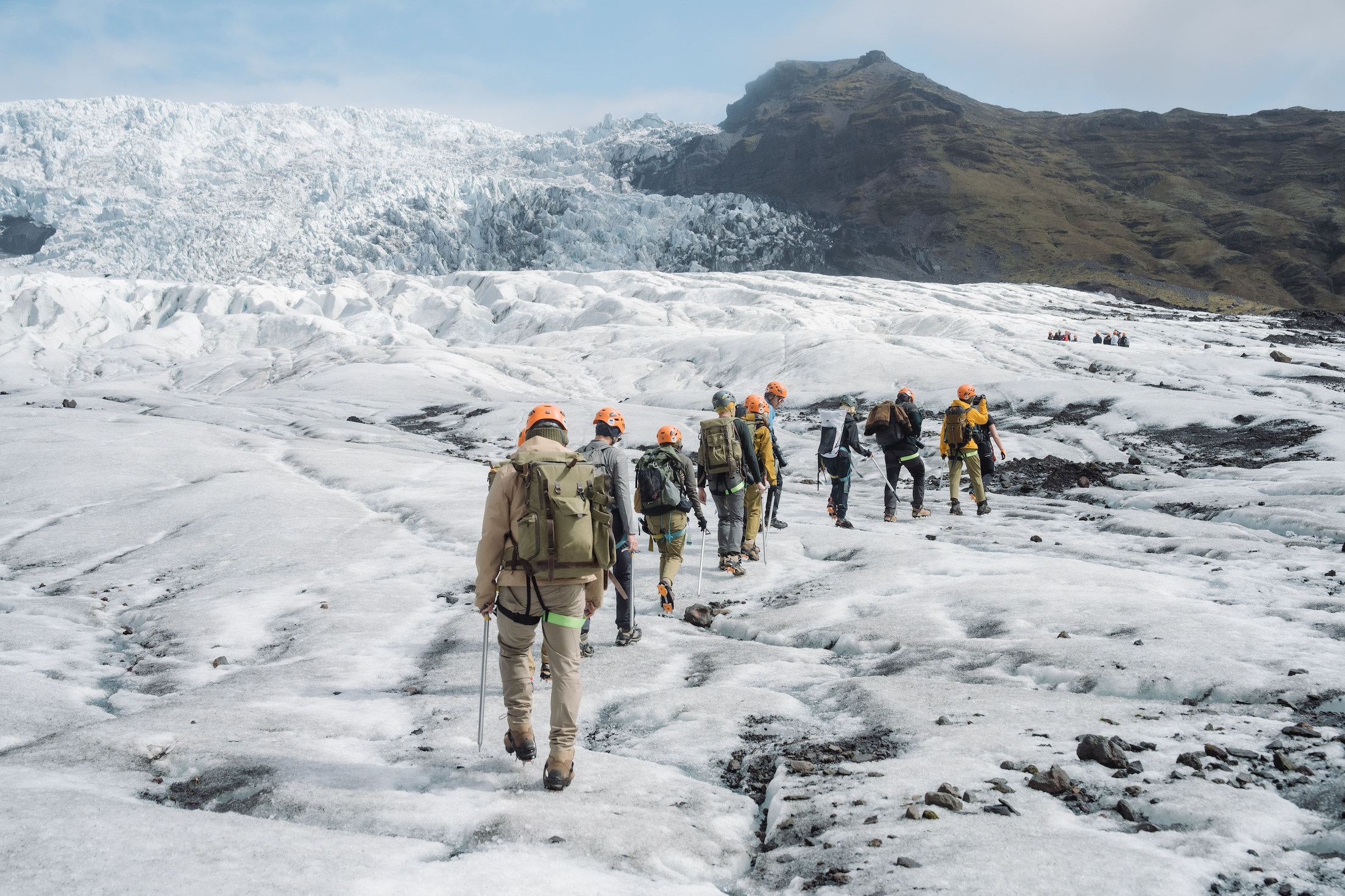 A group of people with backpacks, sticks and helmets trekking across an icy terrain