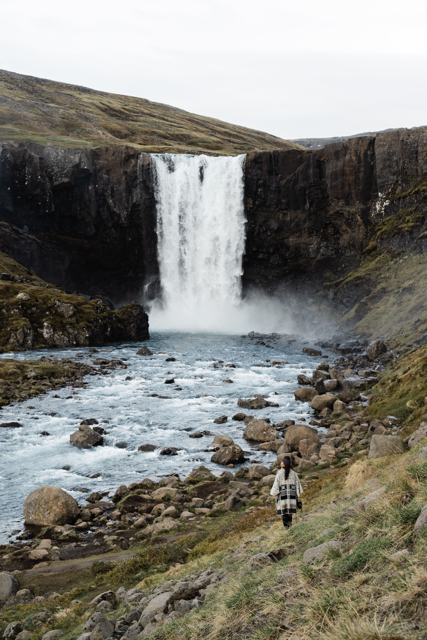 Woman standing on a grassy area, near the base of a big waterfall