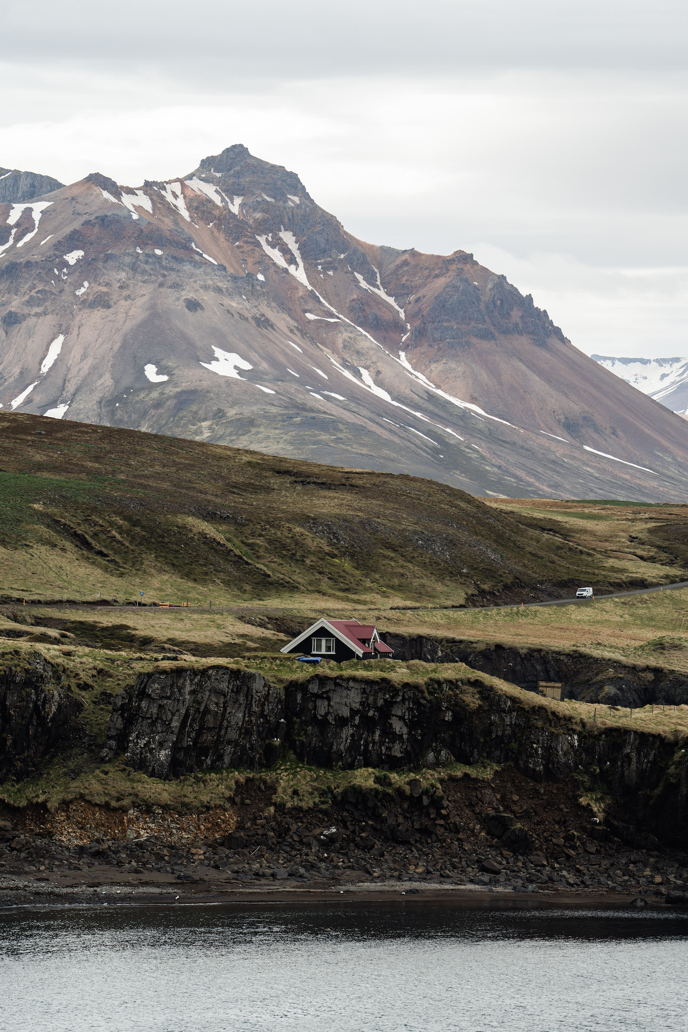 A glimpse of an upper part of a red house along a cliff from a distance, with mountains in the background