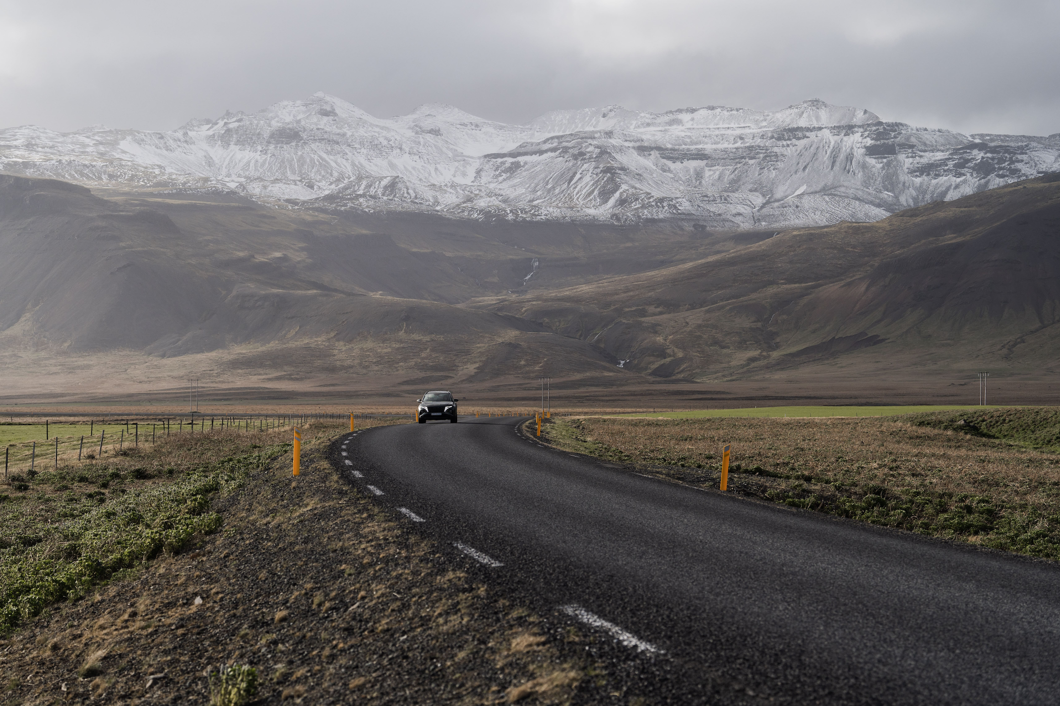 Low-angle view of a car driving on a road along wide fields, with mountains in the background