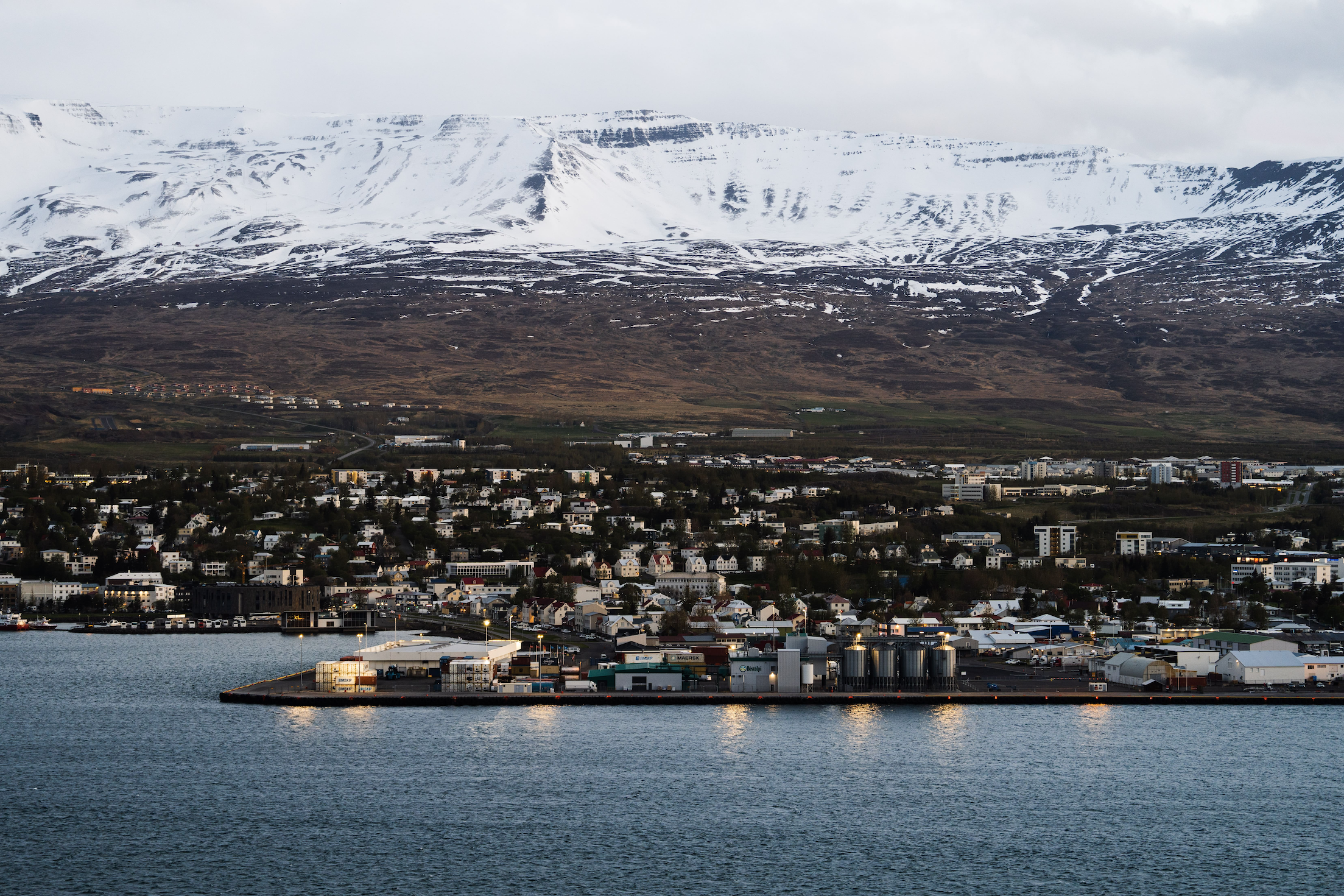 Wide shot of a bright city by the sea with snowy mountains in the background