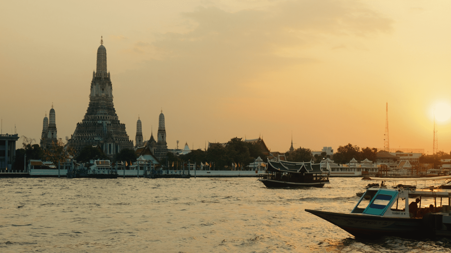 Chao Phraya River at dusk, with some boats along the river and the Wat Arun Temple in the background