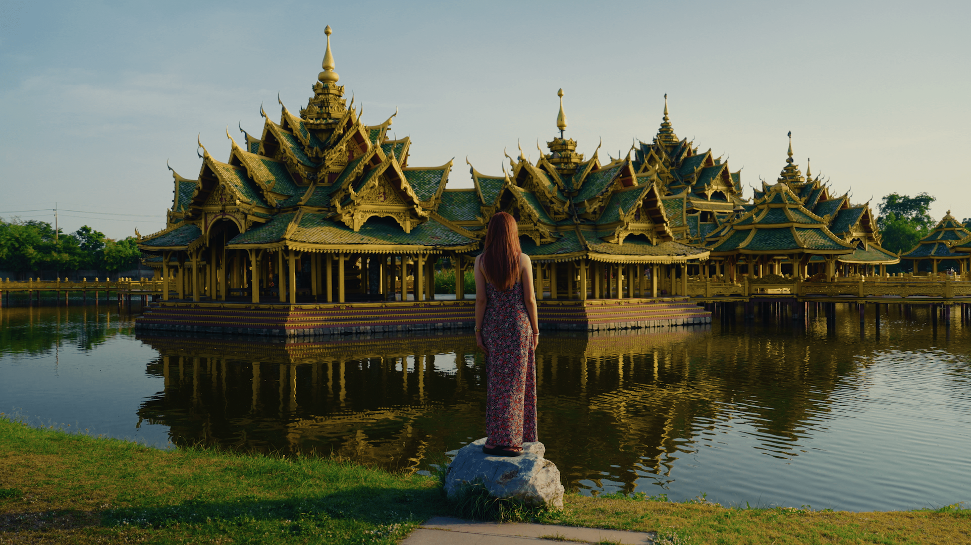 Woman in a long floral dress standing in front of a large Thai pavilion, with her back to the camera