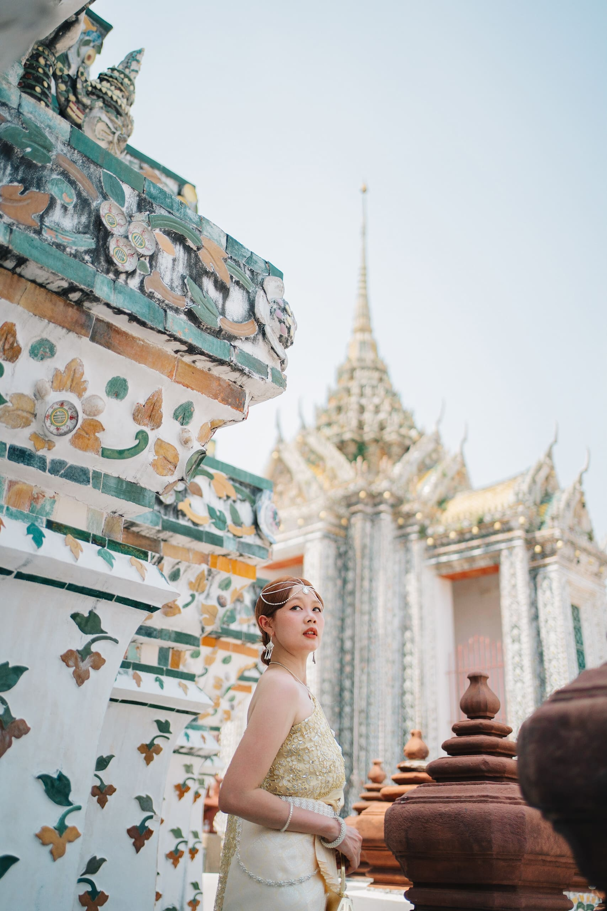 Woman wearing traditional Thai outfit standing amidst and looking up at the tall temple structures