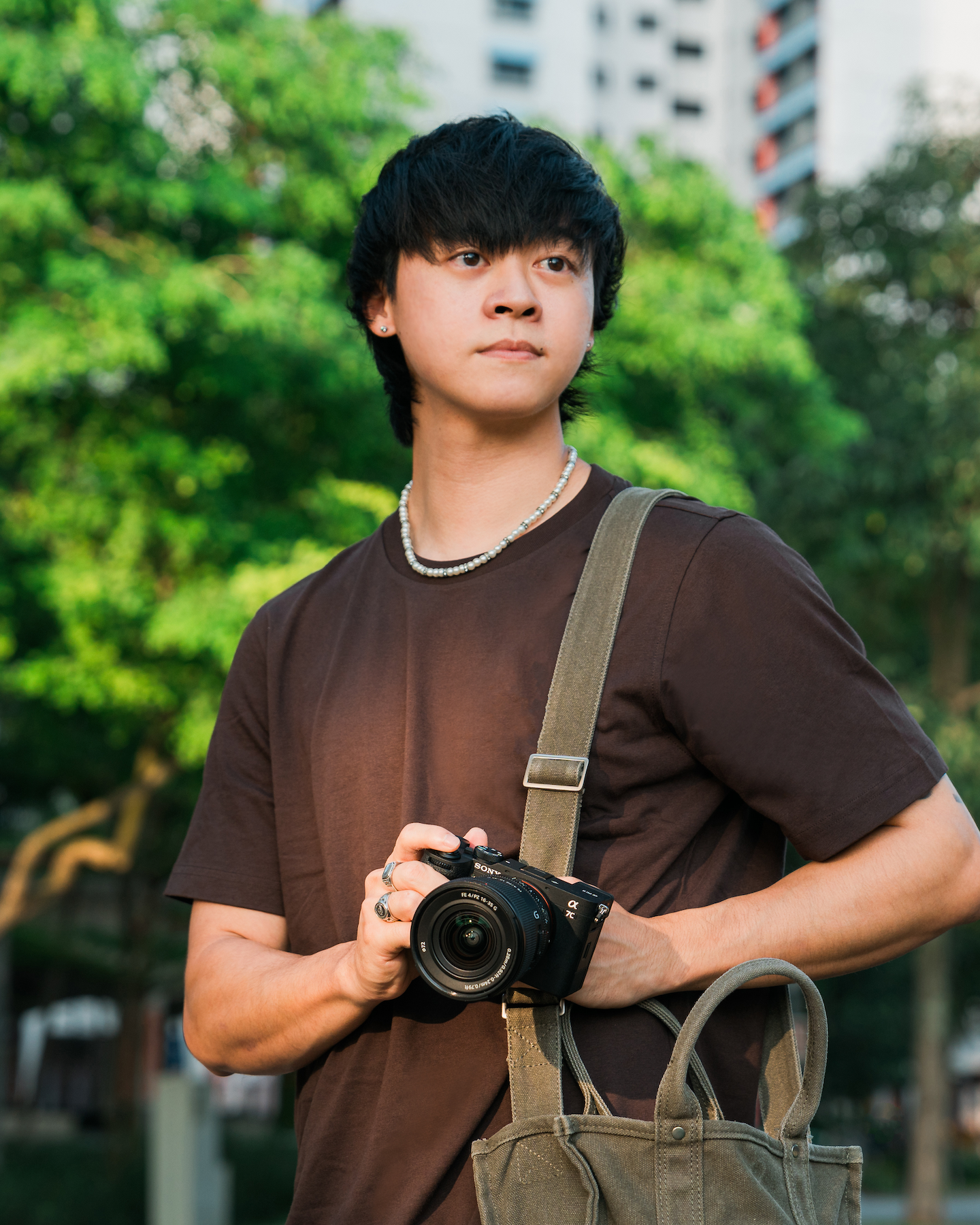 Man in a brown shirt holding a Sony Alpha camera and a deep green shoulder bag, looking to the side